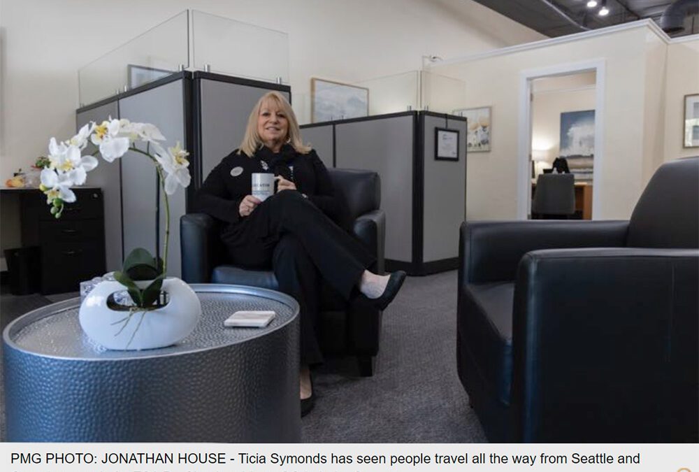 Ticia Symonds sitting in office lobby comfortably chair with coffee and an orchid on the coffee table
